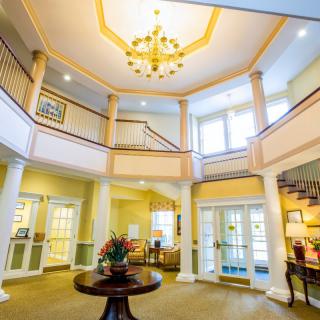 A spacious and elegant lobby with a grand staircase and chandelier, filled with natural light.