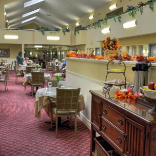 An elegantly decorated dining room with autumn-themed decorations, featuring tables and chairs under warm indoor lighting.