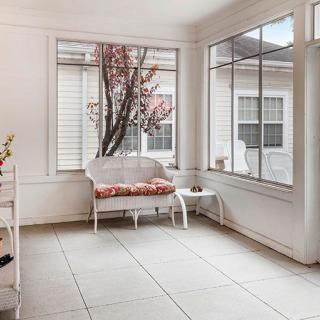 A bright and cozy sunroom with a white bench and large windows showcasing a flowering tree.