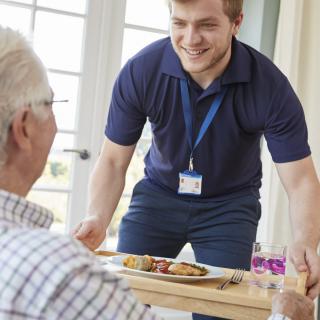 A caregiver serves a meal to an elderly person at home.