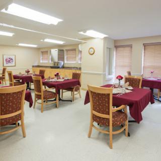 A cozy dining area featuring tables with red tablecloths and wooden chairs, illuminated by bright overhead lights.
