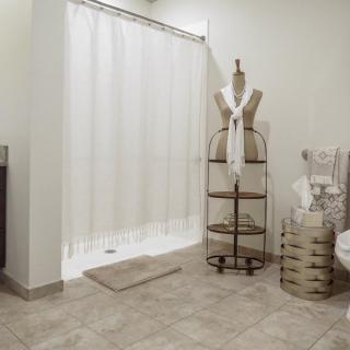 A clean and modern bathroom featuring a white shower curtain, neatly arranged towels on shelves, and a mannequin used for decoration.