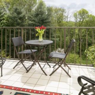 A cozy balcony with a table, chairs, and a vase of flowers overlooking a lush landscape.