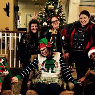 A group of people in festive clothing celebrating Christmas indoors near a decorated tree.