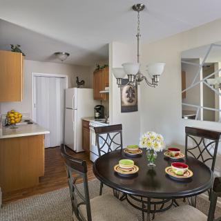 A cozy kitchen and dining area with a round table set for four, featuring a chandelier and decorative flowers.