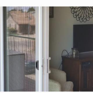 A sliding screen door opens to reveal a cozy living room with a television and furniture, with a balcony visible outside.