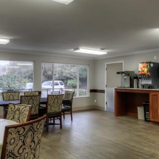 A spacious dining area with tables and chairs, featuring large windows and a coffee station.