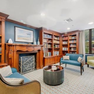 A cozy library with built-in bookshelves and a seating area surrounding a decorative fireplace.