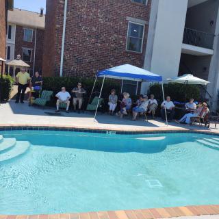 A group of people relaxing by the poolside under umbrellas at an apartment complex.