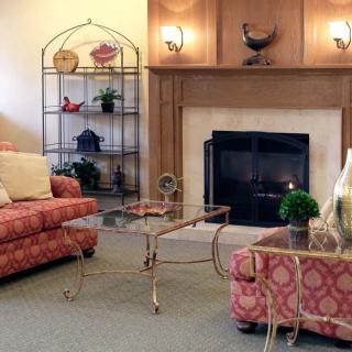 A cozy living room featuring a fireplace, patterned sofas, a glass coffee table, and decorative shelving.