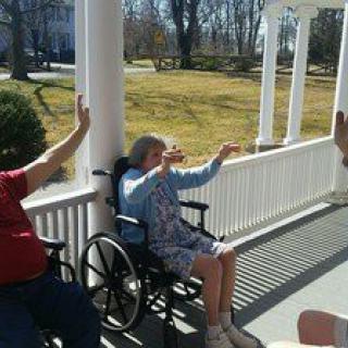 Elderly individuals enjoying a sunny day on the porch, sitting and raising their arms.