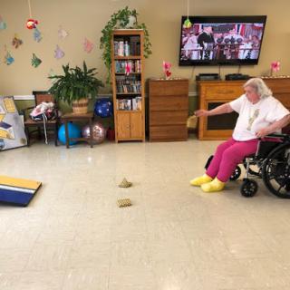 An elderly woman in a wheelchair participates in a game activity in a cheerful indoor setting.