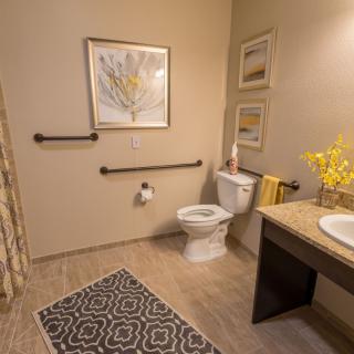 An accessible bathroom with a toilet, sink, and grab bars, decorated with artwork and flowers.