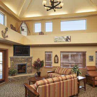 A cozy living room with a high ceiling, featuring a stone fireplace, striped sofas, and rustic decor.
