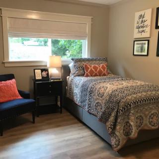 A cozy bedroom with a single bed, decorative pillows, and a bedside table topped with a lamp.