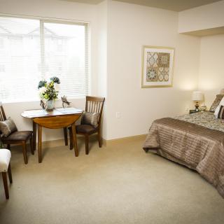 A cozy bedroom with a bed, table, and chairs by the window.