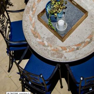 Aerial view of a round patio table with blue cushioned chairs and a decorative centerpiece featuring plants and a candle.