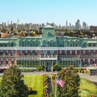 A historic building with a city skyline in the background, surrounded by well-maintained gardens.