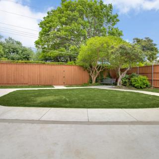 A well-maintained backyard with a lawn, trees, and a wooden fence.