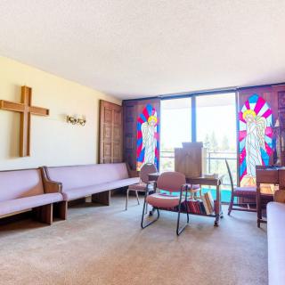A small chapel interior with a cross on the wall and colorful stained glass windows.