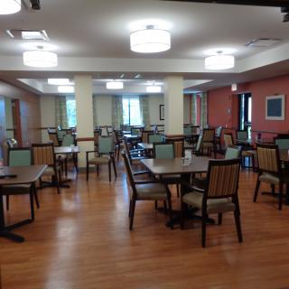 An empty dining room with neatly arranged tables and chairs, featuring a wooden floor and soft overhead lighting.