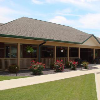 A residential building with a spacious porch, surrounded by a well-maintained garden and lawn.