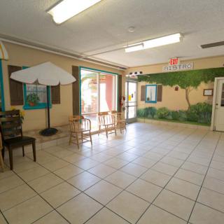 A bright waiting area with tiled flooring, tables, chairs, an umbrella, and a mural on the wall.