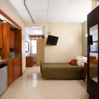 A compact studio apartment featuring a kitchenette and a sleeping area with a wall-mounted TV.