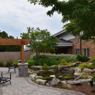 A beautifully landscaped garden featuring a stone pathway, pergola, pond, and seating area.