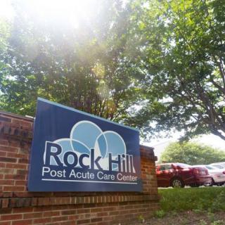 Rock Hill Post Acute Care Center sign on a brick wall surrounded by trees.