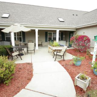 A cozy outdoor patio with seating, tables, and surrounding landscaping.