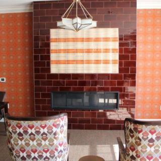 A cozy living room featuring a tiled fireplace with patterned chairs and orange wallpaper.