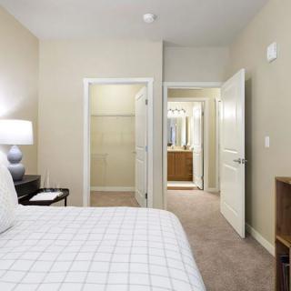 A neatly arranged bedroom with a bed, nightstand, and open doors leading to a closet and bathroom.