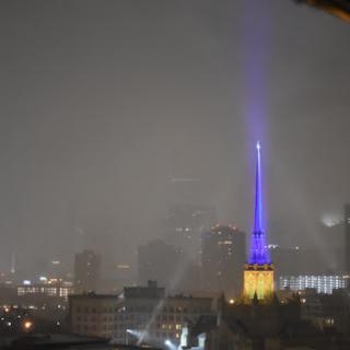 A misty night view of a city skyline illuminated by colorful lights amidst rain.