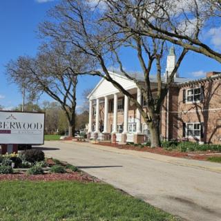 A large building with columns and a sign in front, surrounded by trees and a neatly landscaped area.