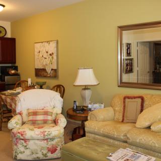 A cozy living room with a floral armchair, yellow sofa, and various decorative elements.