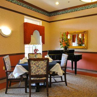 A cozy dining area with a table set for four, decorated with flowers and featuring a grand piano.