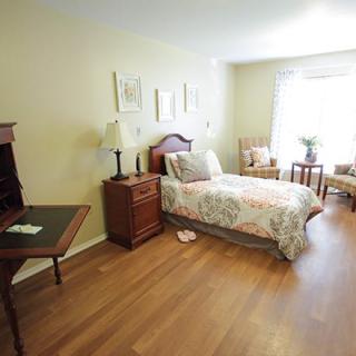 A cozy bedroom with a single bed, desk, and a large window letting in natural light.