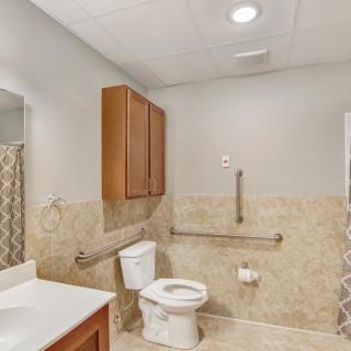 A modern, accessible bathroom featuring a toilet, sink, cabinet, and grab bars.