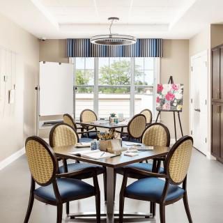 A well-lit meeting room with multiple tables and chairs, equipped with a flip chart and art supplies.