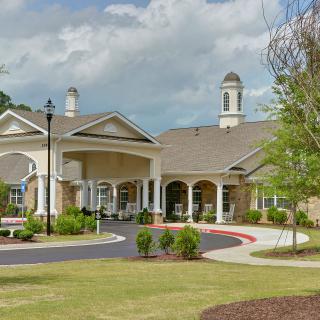 A large, elegant building surrounded by a landscaped garden under a partly cloudy sky.