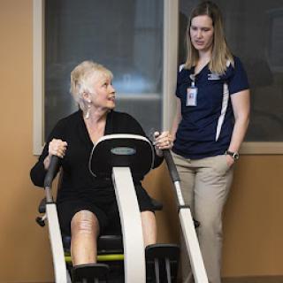 An elderly woman engages in a fitness exercise with the guidance of a trainer.