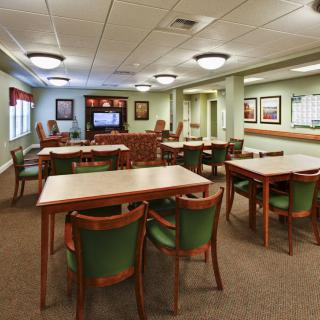 A well-lit meeting room with multiple tables and chairs, featuring a television and wall decor.