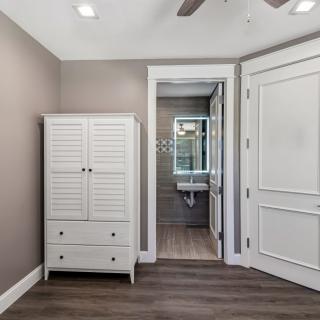 A modern bedroom features a white wardrobe and leads into an attached bathroom with wood flooring and neutral tones.