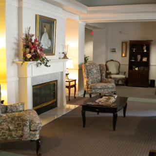 A cozy living room with traditional decor, featuring a fireplace, elegant chairs, and artwork on the walls.