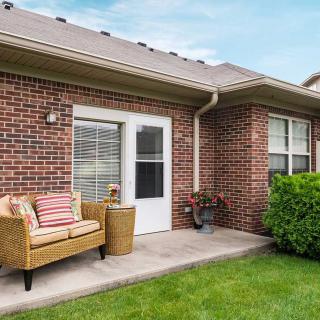 A cozy patio with outdoor seating against a brick house, surrounded by a well-maintained lawn.