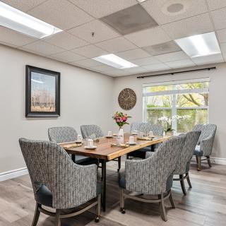 A well-lit dining or meeting room with a large wooden table and cushioned chairs.