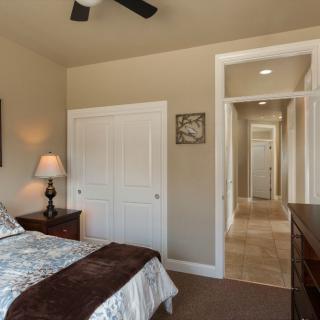 A cozy bedroom with a neatly made bed, bedside lamp, and an open view to a hallway.