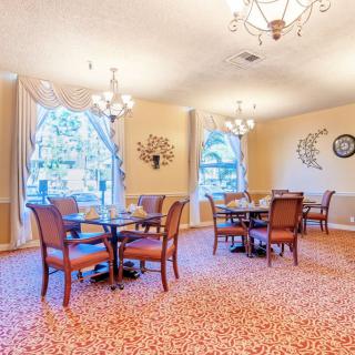 A cozy dining room with elegant chandeliers, neatly arranged tables, and upholstered chairs.