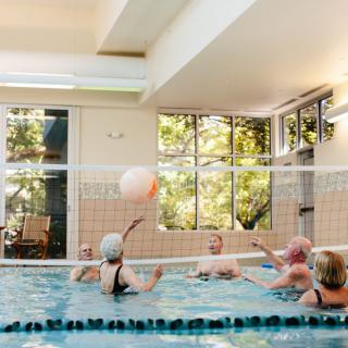 A group of elderly individuals playing water volleyball in an indoor pool.